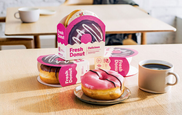 Pöydällä kuorrutettuja donitseja kartonkipakkauksessa.