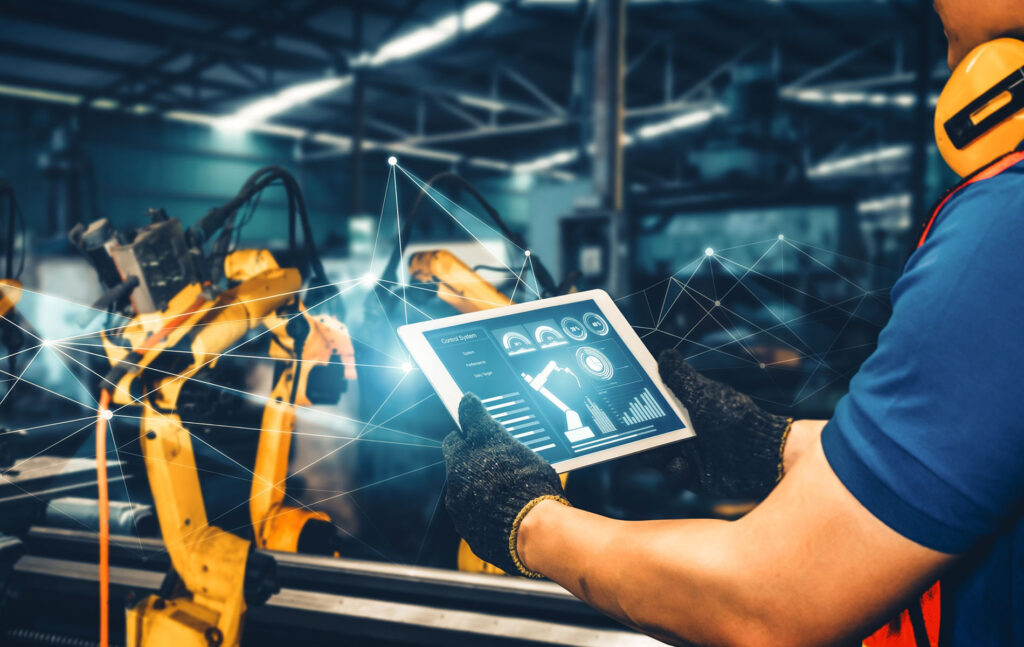 Työntekijä käyttää tablettia ohjatakseen teollisuusrobotteja älytehtaassa, jossa hyödynnetään tekoälyä.