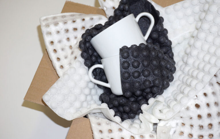 Kaksi valkoista posliinikuppia on pakattu selluloosapohjaiseen, kuplamaisesti muotoiltuun pakkausvaahtoon pahvilaatikossa.