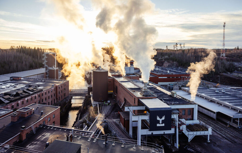 Ilmakuva Metsä Boardin teollisuuslaitoksesta, jonka rakennuksista nousee höyryä metsämaisemassa.