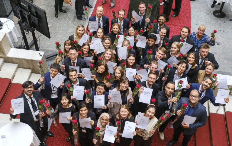 Joukko ihmisiä poseeraa stipendit ja ruusut kädessä