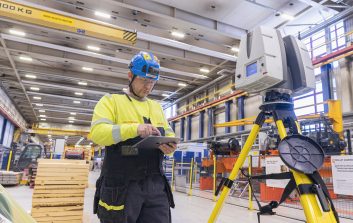 Henkilö tarkistaa mittalaitteella nosturiradan kuntoa teollisuushallin sisällä.