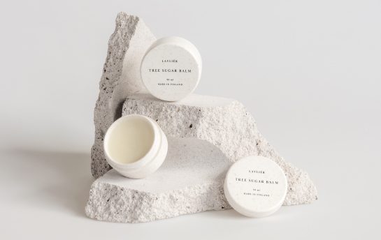 Kolme Lavliér Tree Sugar Balm -voidepurkkia aseteltuna vaaleiden, rosoisten luonnonkivien päälle valkoisella taustalla.