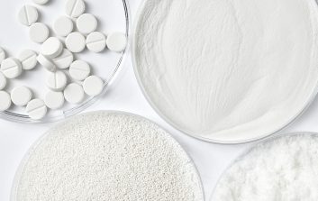 Mikrokiteinen selluloosa jauheena, rakeina ja tabletteina laboratoriomaljoissa valkoisella taustalla