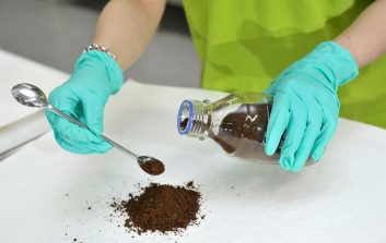 Suojakäsineisiin puetut kädet käsittelevät ruskeaa ligniinijauhetta laboratoriopöydällä